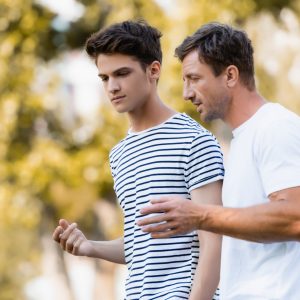Father,Gesturing,And,Talking,With,Teenager,Son,In,Park